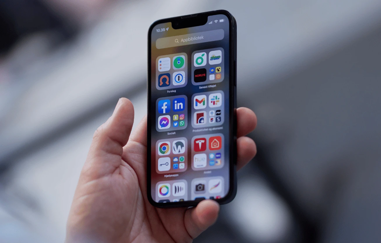 A hand holding a phone showing an app library full of apps.